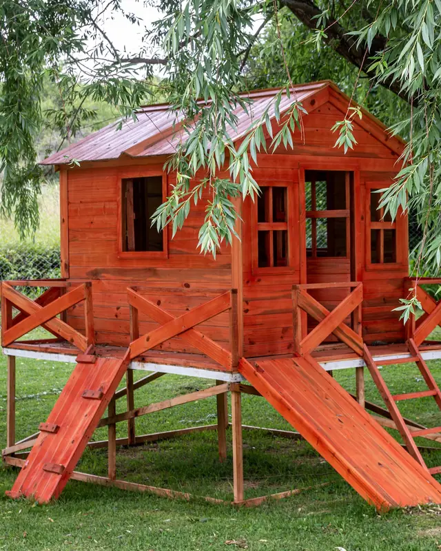 Casita de juegos de madera con tobogán bajo un sauce